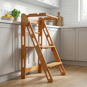 May include: A wooden kitchen step stool with a natural finish. The stool has a ladder-like design with multiple steps and a safety bar at the top. It is designed to help children reach countertops and other elevated surfaces.