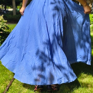 May include: A long, flowing blue skirt with a gathered elastic waistband. The skirt features a lightweight, slightly textured fabric that drapes loosely, creating a full, voluminous silhouette that extends down to the lower leg area.