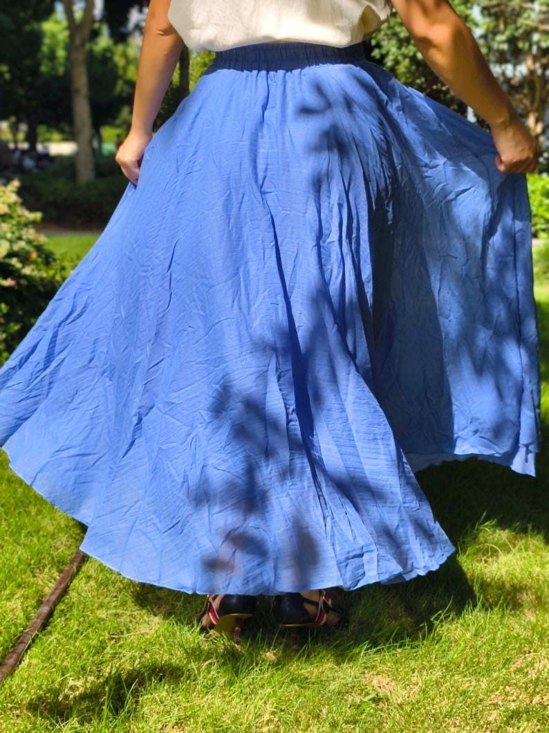 May include: A long, flowing blue skirt with a gathered elastic waistband. The skirt features a lightweight, slightly textured fabric that drapes loosely, creating a full, voluminous silhouette that extends down to the lower leg area.