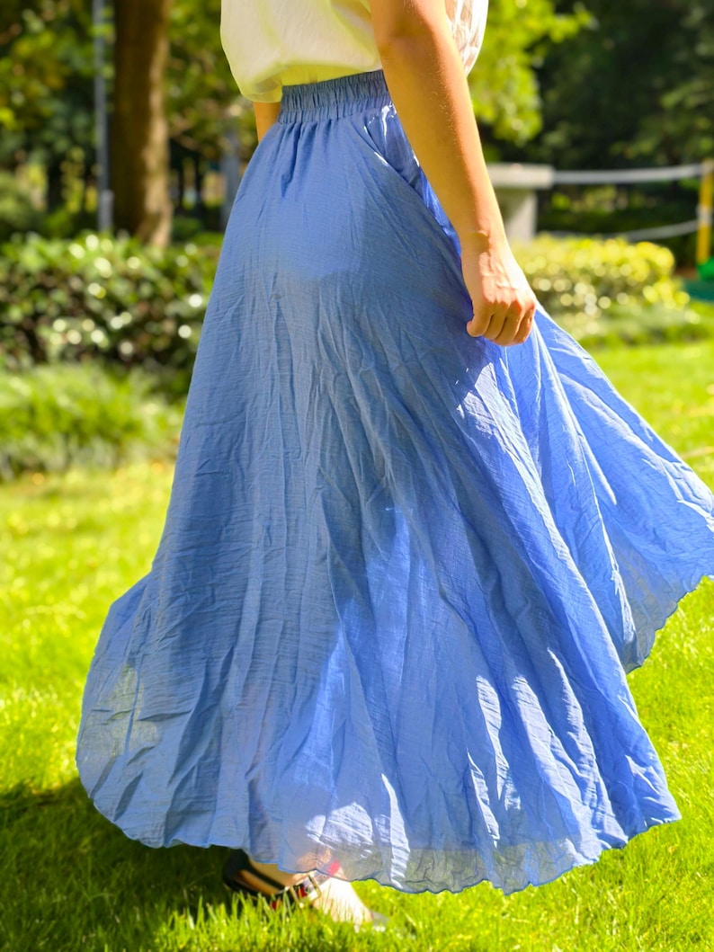 May include: A flowy, cornflower blue midi skirt featuring an elasticated waistband and a lightweight, slightly textured fabric. The skirt has a full, flared silhouette that falls below the knees, providing a loose and comfortable fit for daily wear.