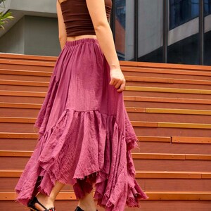 May include: A woman wearing a brown tube top and a flowing, dusty rose skirt with ruffled layers. She is also wearing black heels with red and white accents. The outfit is styled on a set of wooden stairs.