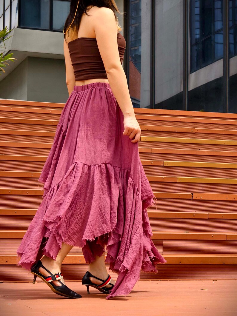 May include: A woman wearing a brown tube top and a flowing, dusty rose skirt with ruffled layers. She is also wearing black heels with red and white accents. The outfit is styled on a set of wooden stairs.