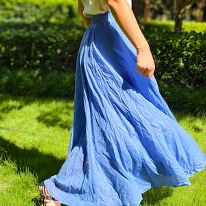 May include: A long, flowing blue skirt with a gathered elastic waistband, paired with a sleeveless white top. The skirt features a crinkled texture and a full, flared silhouette that extends to the ankles, creating a soft and voluminous drape.