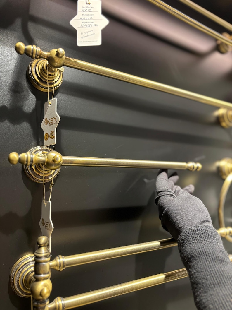 Pode incluir: Toalheiros de lat&atilde;o antigo com detalhes ornamentados. Os toalheiros s&atilde;o montados numa parede cinza escuro. O design inclui suportes circulares decorativos e barras retas para pendurar toalhas. A imagem mostra v&aacute;rios toalheiros.