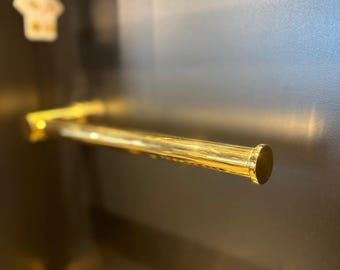 Può includere: Un portasciugamani cilindrico color oro, montato su una superficie scura. La barra ha una finitura liscia e riflettente ed è posizionata orizzontalmente. L'estetica generale suggerisce un moderno e lussuoso accessorio da bagno.
