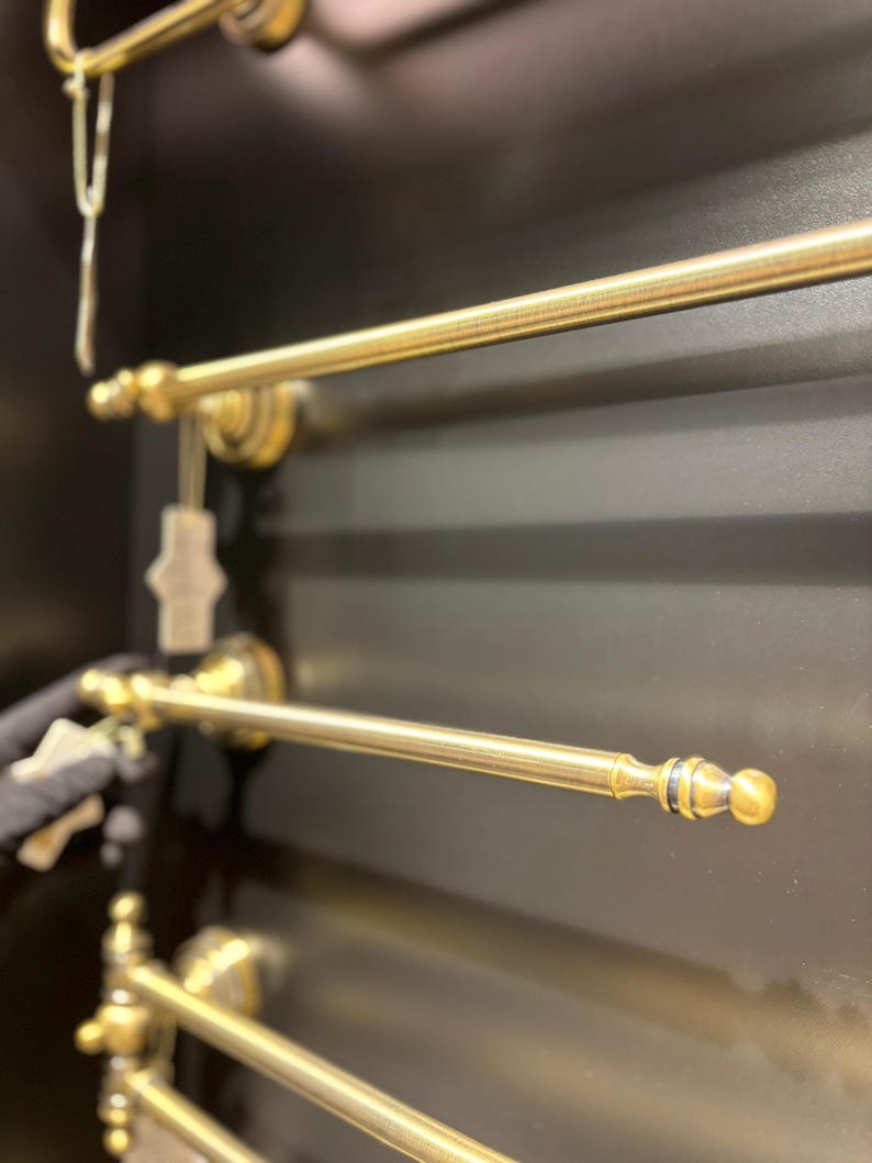 Pode incluir: Close-up de v&aacute;rias barras de toalha de lat&atilde;o antigo montadas em uma superf&iacute;cie escura. As barras t&ecirc;m um design cl&aacute;ssico com pe&ccedil;as decorativas nas extremidades e ferragens de montagem. O acabamento &eacute; dourado envelhecido.
