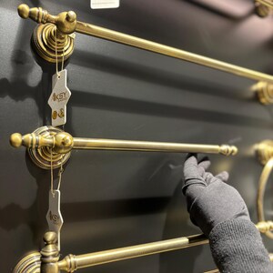 Pode incluir: Toalheiros de lat&atilde;o antigo com detalhes ornamentados. Os toalheiros s&atilde;o montados numa parede cinza escuro. O design inclui suportes circulares decorativos e barras retas para pendurar toalhas. A imagem mostra v&aacute;rios toalheiros.