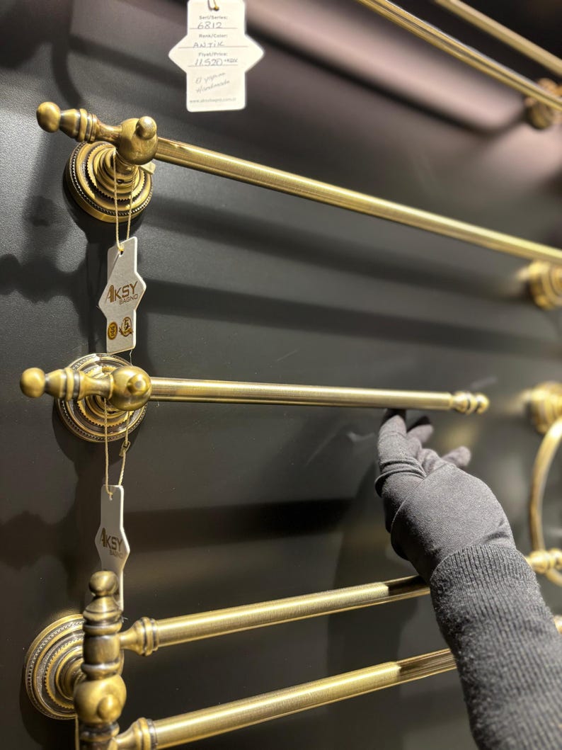 Pode incluir: Toalheiros de lat&atilde;o antigo com detalhes ornamentados. Os toalheiros s&atilde;o montados numa parede cinza escuro. O design inclui suportes circulares decorativos e barras retas para pendurar toalhas. A imagem mostra v&aacute;rios toalheiros.