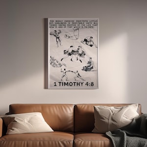 May include: A framed print featuring black and white illustrations of figures in various wrestling poses. The print includes text at the top and the Bible verse 1 Timothy 4:8 at the bottom. The artwork is displayed above a brown leather sofa.