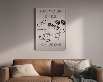 May include: A framed print with the text "FIX YOUR EYES ON JESUS" and various black eyeglasses designs. The print hangs above a brown leather sofa with pillows and a blanket.