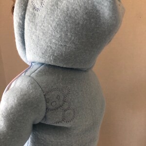 May include: A light blue hooded fleece jacket with a small embroidered bear on the back.