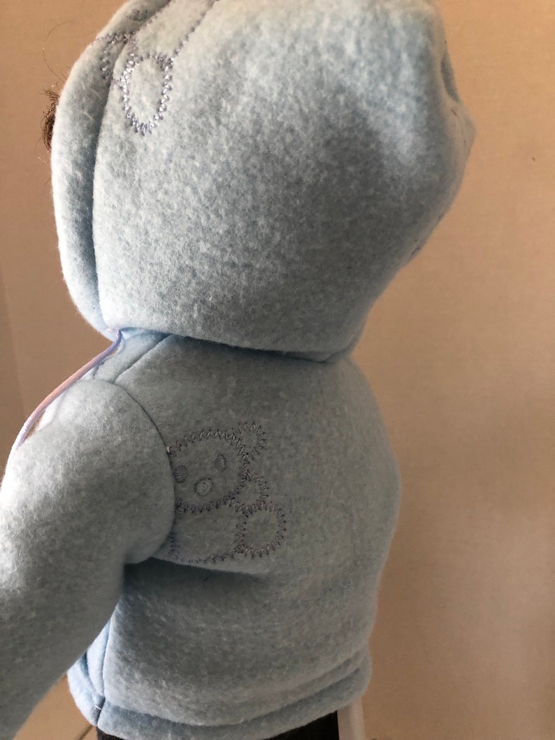 May include: A light blue hooded fleece jacket with a small embroidered bear on the back.