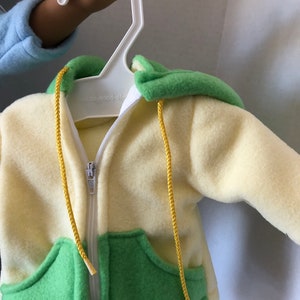 May include: A yellow and green fleece hoodie with a zipper closure and yellow drawstrings. The hoodie has a pocket on each side and the text "our-world-of" is visible on the zipper.