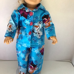 May include: A blue and white pajama set for a doll, featuring a snowflake pattern and images of Elsa, Anna, and Olaf from the movie Frozen.