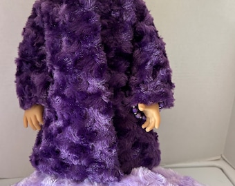 May include: A purple plush coat with a swirl pattern. The coat is worn by a doll with blonde hair. The doll is wearing a matching purple skirt.