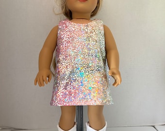 May include: A doll wearing a sleeveless iridescent dress with a pink and white color gradient. The dress has a mosaic-like pattern. The doll is wearing white boots.