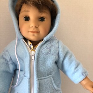 May include: A light blue fleece jacket with a white zipper and a hood. The jacket has embroidered white flowers on the front and pockets on the sides.