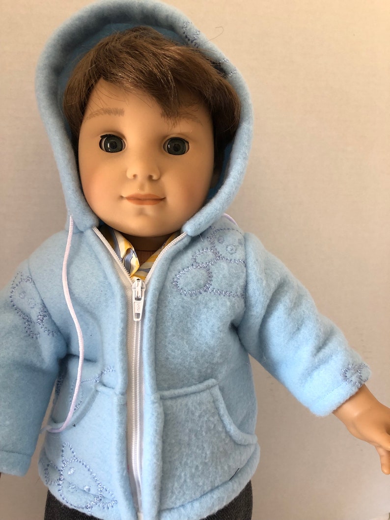 May include: A light blue fleece jacket with a white zipper and a hood. The jacket has embroidered white flowers on the front and pockets on the sides.