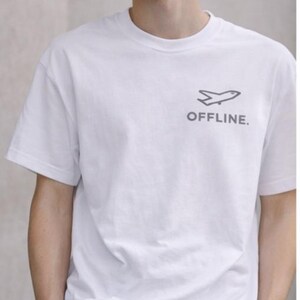 Puede incluir: Camiseta blanca con un gr&aacute;fico de avi&oacute;n gris y la palabra "OFFLINE". El conjunto incluye pantalones negros y una gorra de b&eacute;isbol negra.