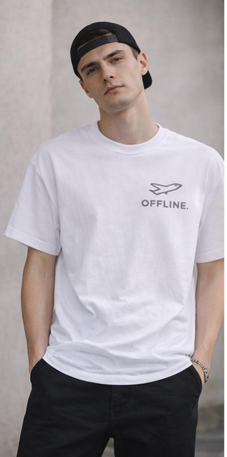Puede incluir: Camiseta blanca con un gr&aacute;fico de avi&oacute;n gris y la palabra "OFFLINE". El conjunto incluye pantalones negros y una gorra de b&eacute;isbol negra.