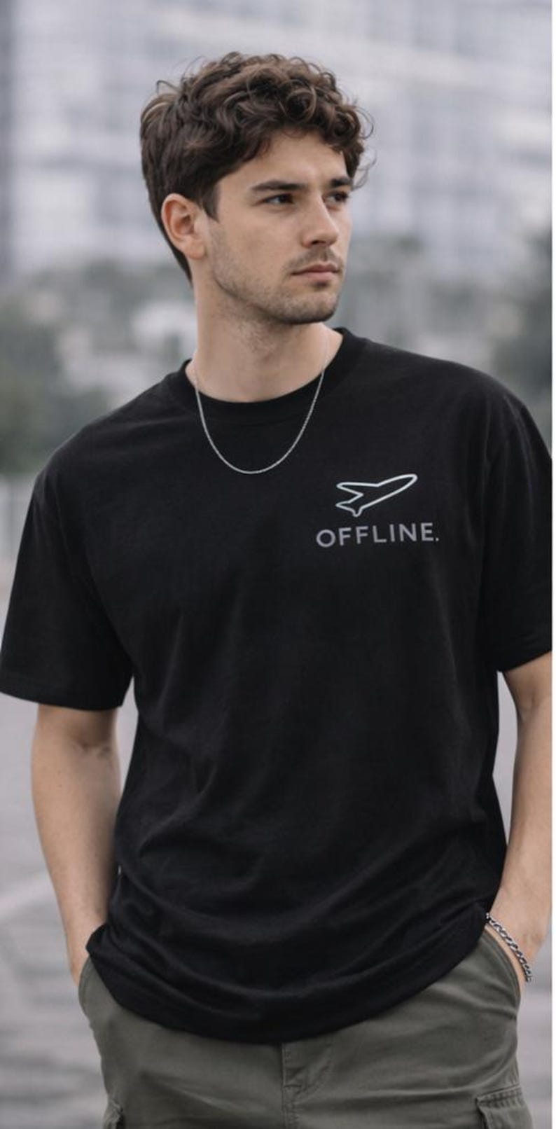 Puede incluir: Camiseta negra con un gr&aacute;fico de avi&oacute;n blanco y la palabra "OFFLINE". El modelo lleva una cadena y una pulsera de plata. Los pantalones son de color verde oliva. Estilo casual y moderno.