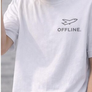 Puede incluir: Camiseta blanca con un gr&aacute;fico de avi&oacute;n gris y la palabra "OFFLINE." impresa debajo. La camiseta est&aacute; hecha de un material suave y tiene mangas cortas.