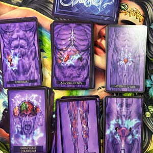 May include: A collection of tarot cards with purple and white illustrations of the human anatomy. The cards feature images of the abdomen, brain, and legs, with Russian text. A deck of cards with a blue and white design is at the top.