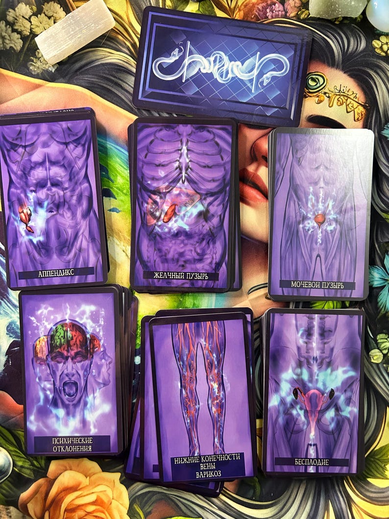 May include: A collection of tarot cards with purple and white illustrations of the human anatomy. The cards feature images of the abdomen, brain, and legs, with Russian text. A deck of cards with a blue and white design is at the top.