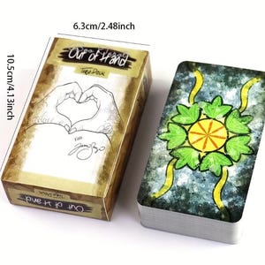 May include: A tarot deck with a box labelled "Out of Hand Tarot Deck." The box is 6.3cm wide and 10.5cm tall, with a design of hands forming a heart. The deck's back has a green and yellow floral design.