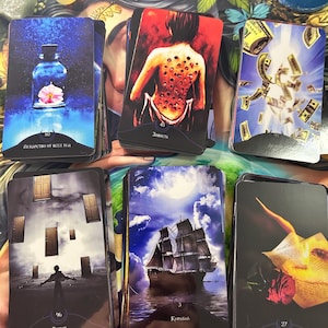 Könnte beinhalten: Eine Sammlung von Tarotkarten mit verschiedenen Illustrationen. Eine Karte zeigt eine blaue Flasche mit einer Blume, eine andere zeigt den Rücken einer Person mit Löchern, und andere zeigen ein Schiff, Geld und einen brennenden Brief. Die Karten haben russischen Text.