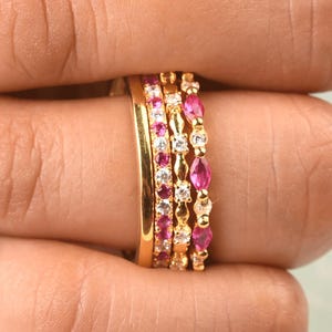 Puede incluir: Un conjunto de cuatro anillos de oro usados juntos. El set incluye una banda de oro pulido liso, una banda con pequeñas piedras rosas redondas, una banda con piedras claras redondas alternadas y una banda con piedras rosas de corte marquesa.