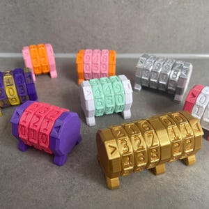 Op de afbeelding: Een verzameling kleurrijke combinatiesloten in verschillende kleuren, waaronder roze, oranje, paars, groen, zilver en goud. Elk slot heeft draaiende schijven met cijfers en symbolen, wat wijst op een puzzel of spel.
