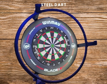 Puede incluir: Un tablero de dardos de acero Winmau Autodarts con un marco azul y un objetivo rojo, verde y negro. El tablero tiene el logotipo de Winmau y el texto "STEEL DART". Dos dardos rojos están en la parte inferior. También se ve el texto "BELEUCHTUNGSRING MIT KAMERAHALTER".