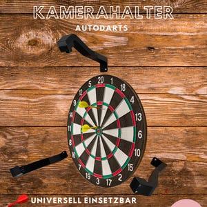 Op de afbeelding: Een dartbord met gele pijlen in het midden, omringd door zwarte camerabevestigingen. De tekst op de afbeelding luidt "universelle KAMERAHALTER AUTODARTS" en "UNIVERSELL EINSETZBAR FÜR 32x32 MM KAMERAS KOMPATIBEL MIT VIELEN BELEUCHTUNGSSYSTEMEN". De achtergrond is een houten oppervlak.