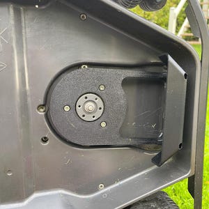 May include: Close-up of a dark gray robotic lawnmower. The image highlights the internal components, including a circular black motor housing secured with screws. The mower's wheel and a portion of the handle are visible.
