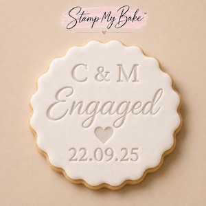 May include: A round scalloped biscuit topped with smooth white icing, embossed with the text C & M, Engaged, a heart icon, and the date 22.09.25. Above the biscuit, the text Stamp My Bake is printed in black on a light pink brushstroke background.