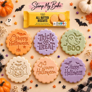 May include: A set of six round biscuits with Halloween-themed embossed designs including ghosts, bats, pumpkins, and text reading Happy Halloween, Trick or Treat, and Boo, arranged below a yellow M&S Food All Butter Biscuits packet.