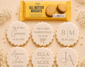 May include: A yellow M&S Food All Butter Biscuits package above six round, scalloped-edge cookies. Each cookie features custom embossed text including names like Mr & Mrs Grove, Barrowdale, Ayman & Aicha, Ella & Alex, and various dates.