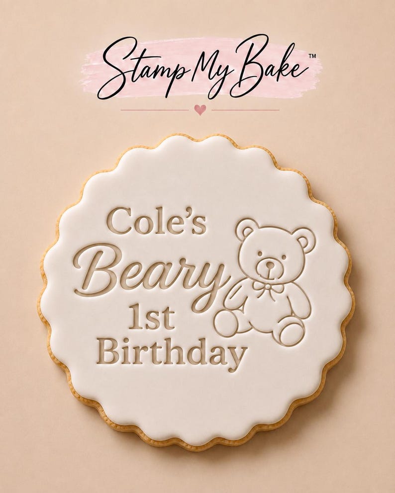May include: A round scalloped cookie with white icing featuring the embossed text 'Cole's Beary 1st Birthday' and a graphic of a teddy bear. Above the cookie, the text 'Stamp My Bake' is displayed with a small heart icon.
