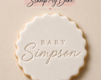 May include: A round scalloped cookie with smooth white icing featuring the embossed text BABY Simpson in the center. Above the cookie, the text Stamp My Bake is displayed in black script with a small pink heart icon below it.
