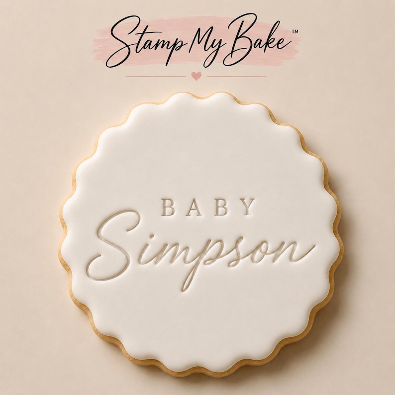 Puede incluir: Una galleta redonda festoneada con glaseado blanco liso que presenta el texto en relieve BABY Simpson en el centro. Sobre la galleta, el texto Stamp My Bake se muestra en letra cursiva negra con un peque&ntilde;o icono de coraz&oacute;n rosa debajo.