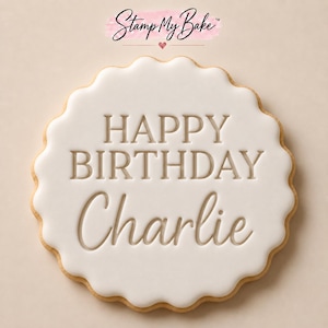 May include: A round, scalloped-edge biscuit topped with smooth white icing. The text HAPPY BIRTHDAY Charlie is embossed into the centre of the icing. Above the biscuit, the text Stamp My Bake is displayed with a small heart icon.
