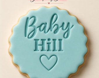 May include: A round scalloped cookie stamp with a light blue surface featuring the embossed text Baby Hill and a heart icon below. The Stamp My Bake logo is visible at the top of the image in black text on a pink brush stroke.