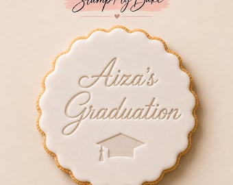 May include: A round scalloped cookie topped with smooth white icing. The text Aiza's Graduation is embossed in the center, accompanied by a graduation cap icon below the text. The brand name Stamp My Bake is visible above the cookie.