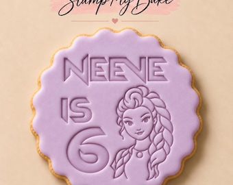 May include: A round, scalloped-edge cookie topped with smooth light purple icing. The icing is embossed with the text "NEEVE IS 6" and a stylized illustration of a person with a long braided hairstyle. The brand name "Stamp My Bake" appears above.