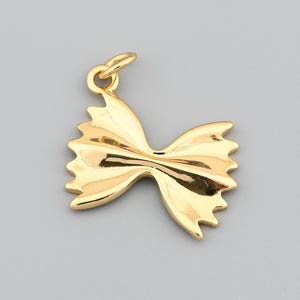 Puede incluir: Un dije de pasta Farfalle de color dorado. El dije es una miniatura detallada de la forma de la pasta, con un lazo en la parte superior para sujetarlo a un collar o pulsera. El dije está hecho de un metal brillante y reflectante.