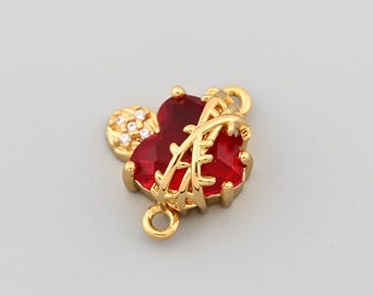 May include: A gold-colored charm with a red heart-shaped gemstone and a small cluster of clear stones. The charm has a decorative design and two loops for attachment, suitable for jewelry making or embellishment.