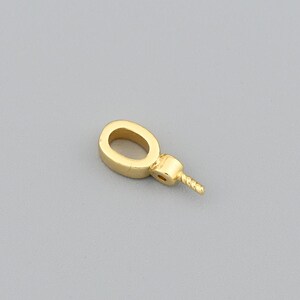 May include: A small, gold-colored jewelry finding with an oval loop and a threaded post. The finding is likely used for attaching beads or other decorative elements to jewelry pieces. The background is a solid, neutral gray.
