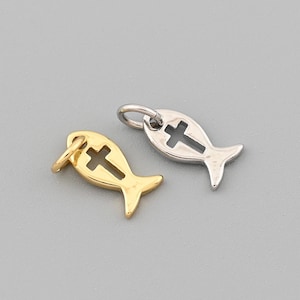 May include: Two small fish-shaped pendants. One is gold-colored, the other is silver-colored. Each pendant has a cross cut out in the center. The pendants are on a gray background.