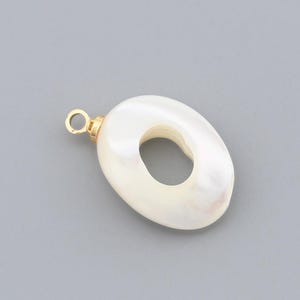 May include: Oval-shaped pendant with a gold-colored loop and a white, pearlescent finish. The pendant has a hole in the center. The jewelry piece is set against a gray background.